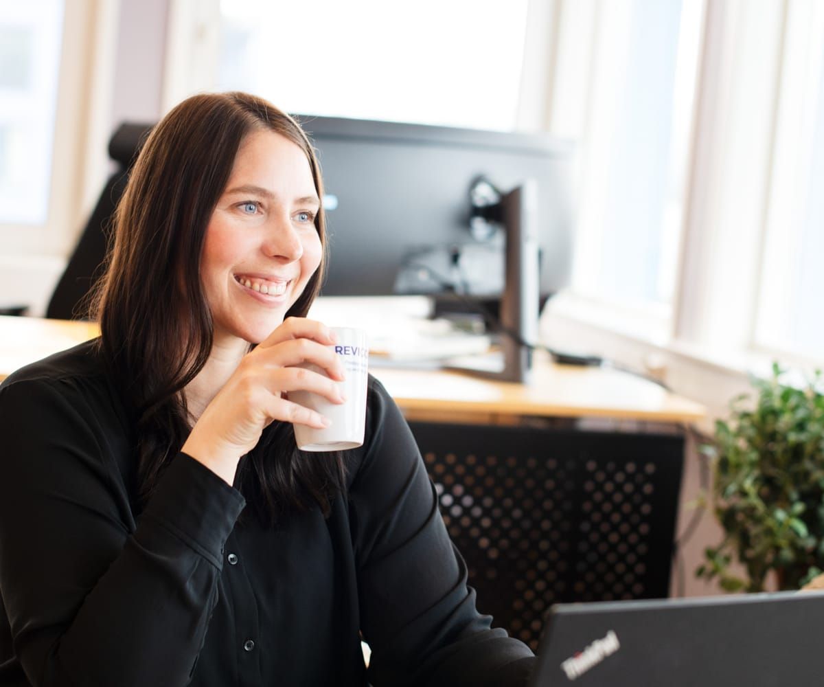 Smilende revisor med en kaffekopp ved skrivebordet